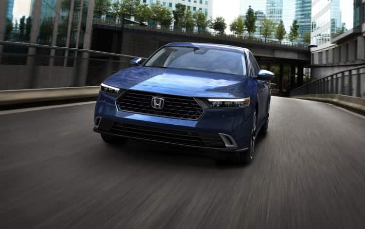 2024 Honda Accord Touring Hybrid in Canyon River Blue Metallic driving down a city street, showing the stylish grille and front end.