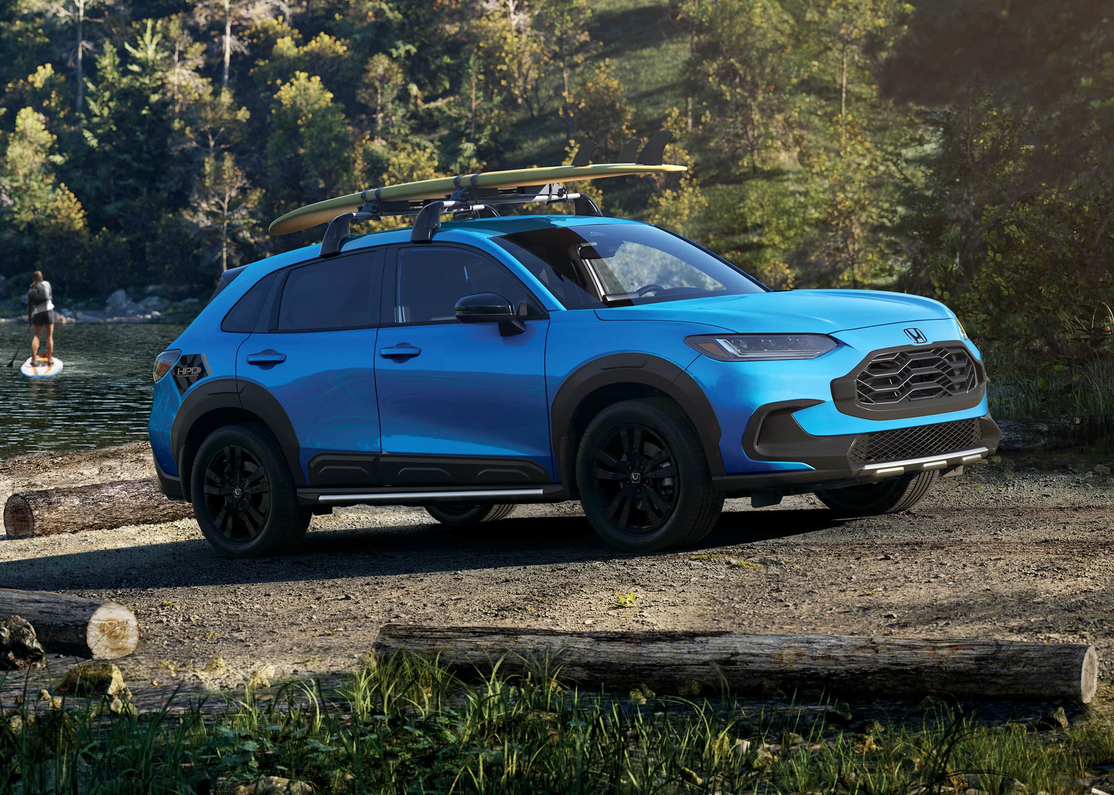 3/4 front passenger-side view of the 2026 Honda HR-V Sport in Boost Blue Pearl, shown parked next to a lake.