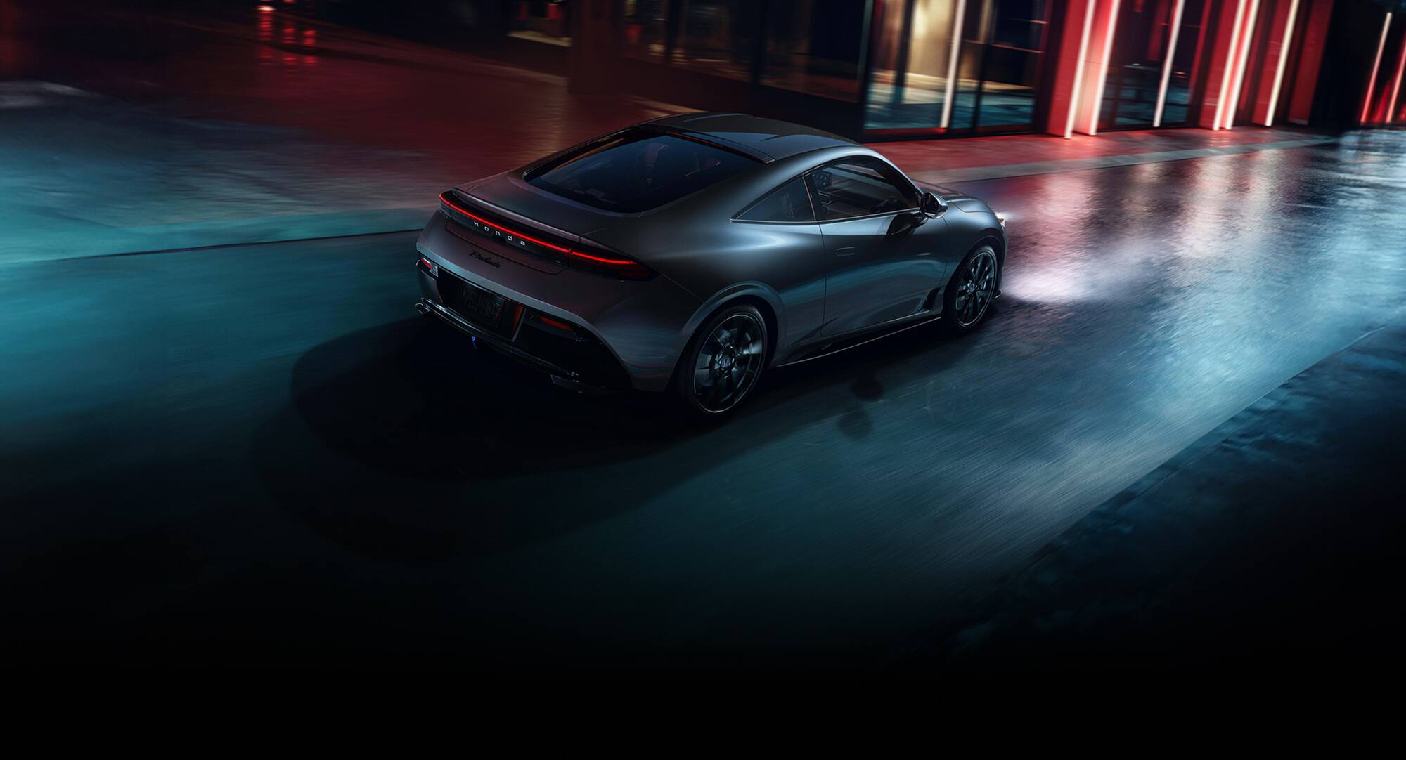 Se muestra la parte posterior de un Honda Prelude Hybrid 2027 en Meteorite Gray Metallic conduciendo por una calle de la ciudad por la noche (estimulante coupé híbrido).