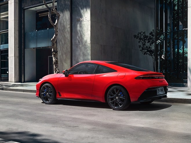 Honda Prelude 2027 en Rallye Red, vista trasera de 3/4, estacionado solo en una calle del centro de la ciudad (coupé híbrido cautivante).